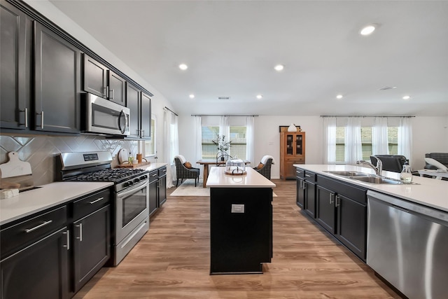 kitchen with sink, tasteful backsplash, light hardwood / wood-style flooring, an island with sink, and appliances with stainless steel finishes