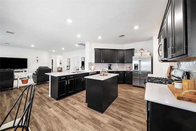 kitchen featuring kitchen peninsula, appliances with stainless steel finishes, sink, light hardwood / wood-style floors, and a kitchen island