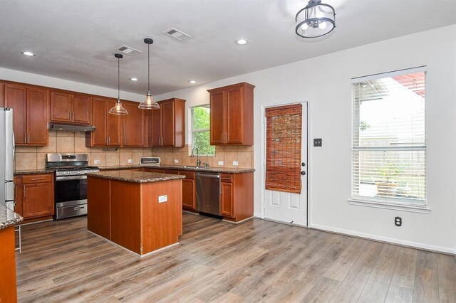 kitchen featuring dark stone counters, a center island, hanging light fixtures, and appliances with stainless steel finishes