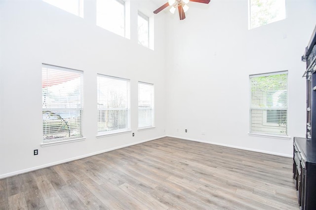 unfurnished living room with plenty of natural light, ceiling fan, light wood-type flooring, and a high ceiling