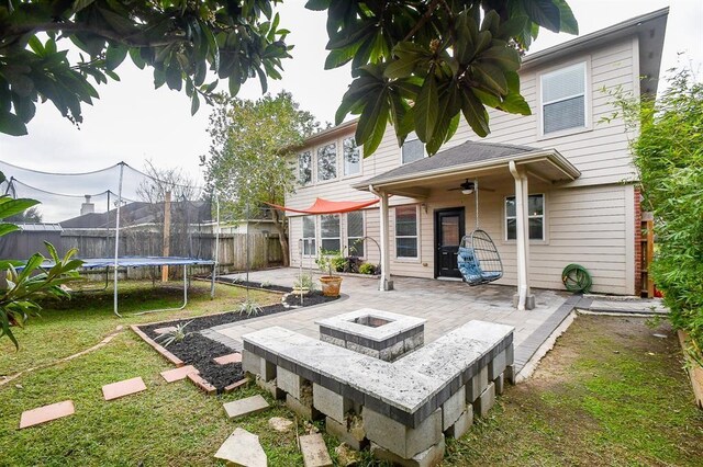 rear view of property featuring a trampoline, ceiling fan, a yard, a patio area, and an outdoor fire pit