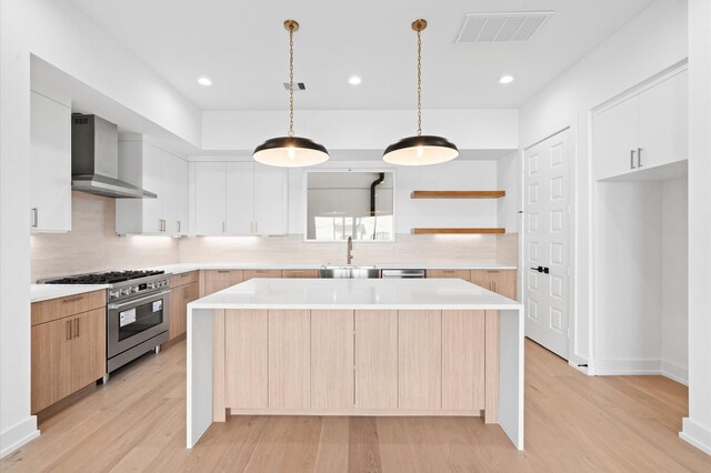 kitchen featuring wall chimney exhaust hood, a kitchen island, white cabinetry, and high end range