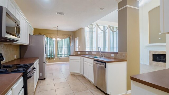 kitchen featuring appliances with stainless steel finishes, sink, white cabinets, hanging light fixtures, and light tile patterned flooring