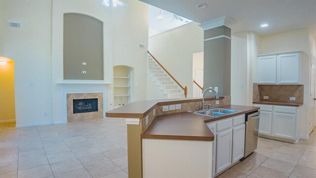 kitchen featuring stainless steel dishwasher, sink, light tile patterned floors, a center island with sink, and white cabinets