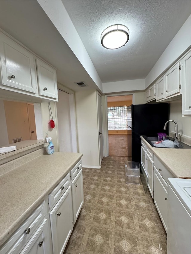 kitchen featuring sink, a textured ceiling, black refrigerator, white cabinets, and range