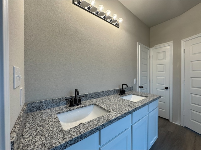 bathroom featuring wood finished floors, double vanity, a textured wall, and a sink