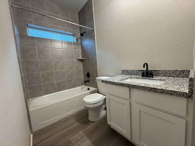 bathroom featuring wood finished floors, a textured wall, toilet, shower / washtub combination, and vanity