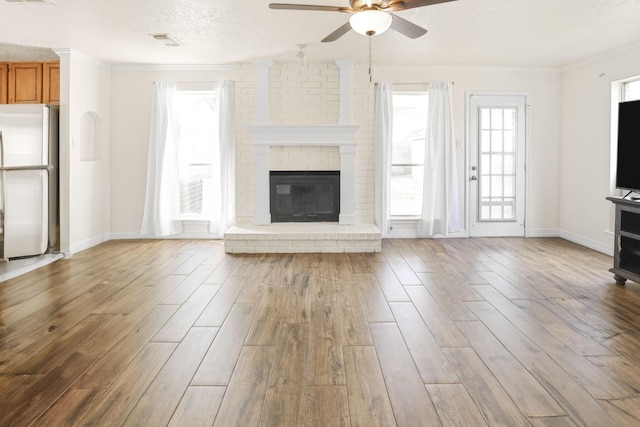 unfurnished living room featuring a textured ceiling, a brick fireplace, ceiling fan, and crown molding