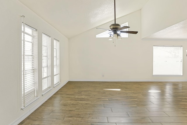 empty room with ceiling fan, a healthy amount of sunlight, lofted ceiling, and dark wood-type flooring