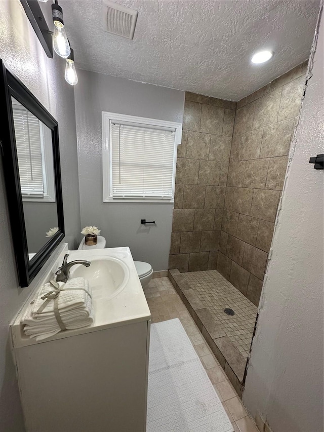 bathroom featuring a tile shower, a textured ceiling, vanity, tile patterned flooring, and toilet