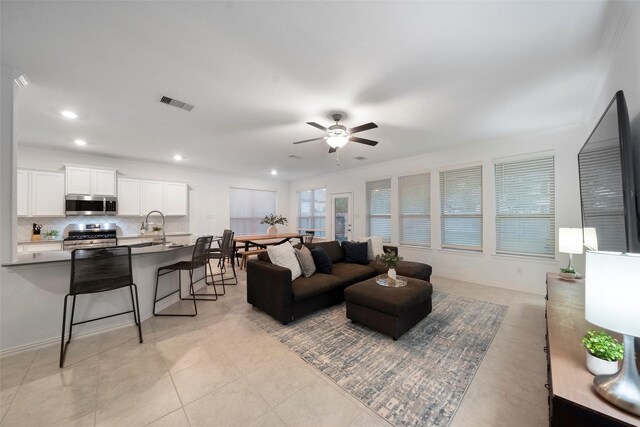 tiled living room with ceiling fan, ornamental molding, and sink