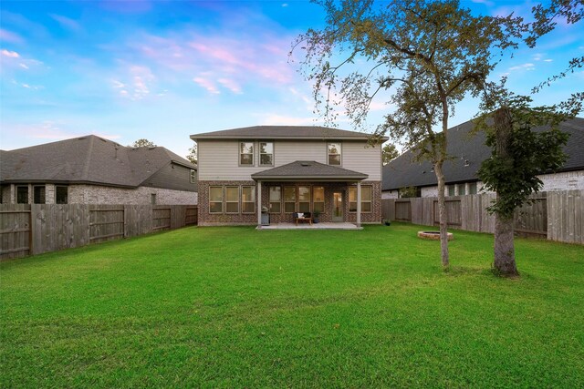 back house at dusk featuring a yard and a patio area