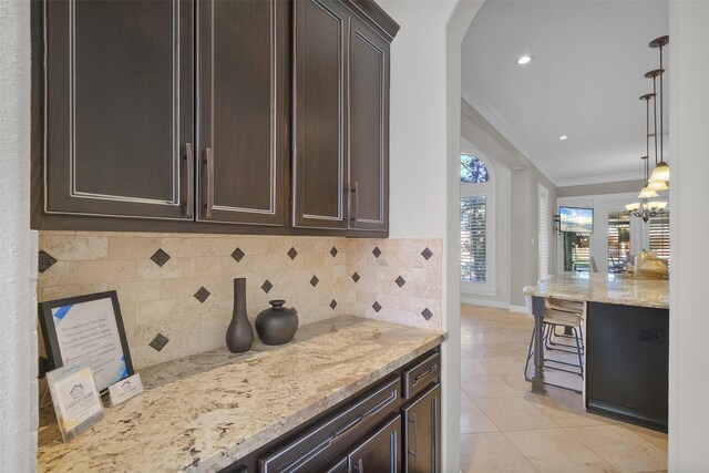 kitchen featuring crown molding, light stone countertops, tasteful backsplash, decorative light fixtures, and dark brown cabinetry