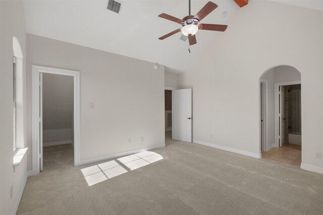 unfurnished bedroom featuring connected bathroom, ceiling fan, high vaulted ceiling, a walk in closet, and light carpet