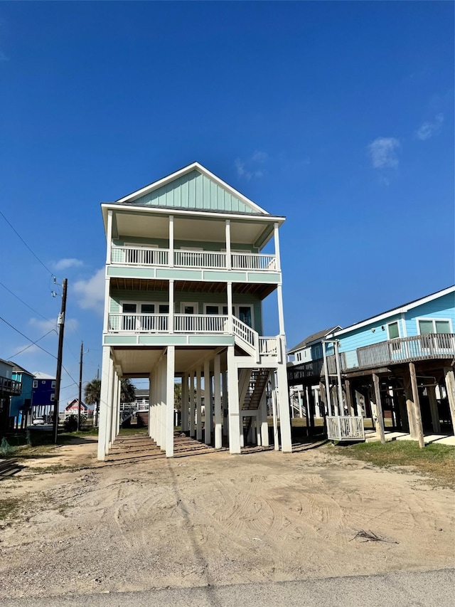 raised beach house with a carport, dirt driveway, stairs, and board and batten siding