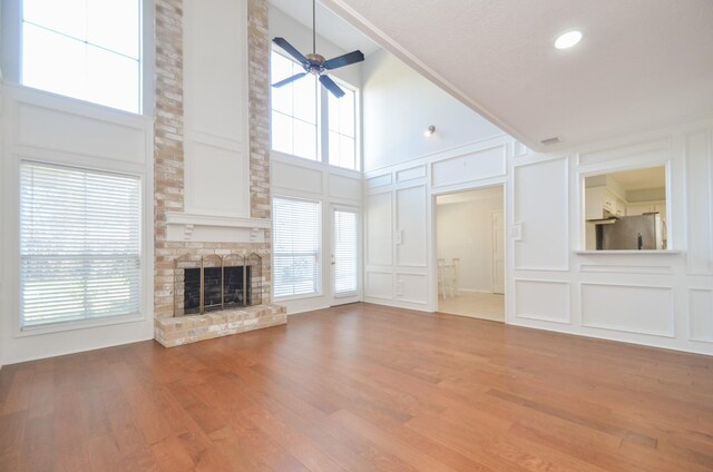 unfurnished living room with ceiling fan, a towering ceiling, wood-type flooring, and a brick fireplace