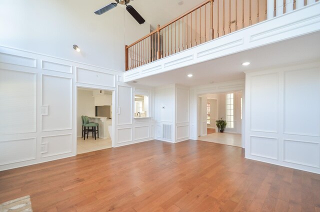 unfurnished living room with a towering ceiling, light hardwood / wood-style floors, and ceiling fan