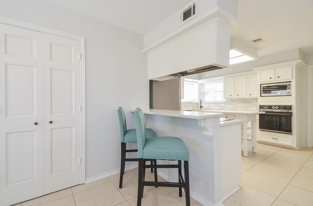 kitchen featuring kitchen peninsula, a kitchen breakfast bar, oven, white cabinetry, and stainless steel microwave