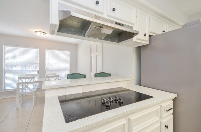 kitchen featuring light stone counters, black electric cooktop, light tile patterned floors, white cabinetry, and stainless steel refrigerator