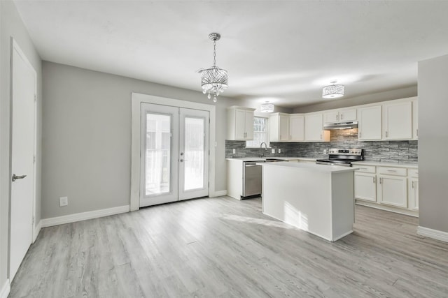 kitchen with appliances with stainless steel finishes, a kitchen island, decorative light fixtures, white cabinetry, and light hardwood / wood-style floors