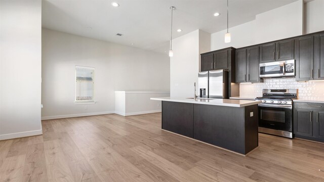 kitchen with decorative backsplash, stainless steel appliances, a center island with sink, light hardwood / wood-style floors, and hanging light fixtures