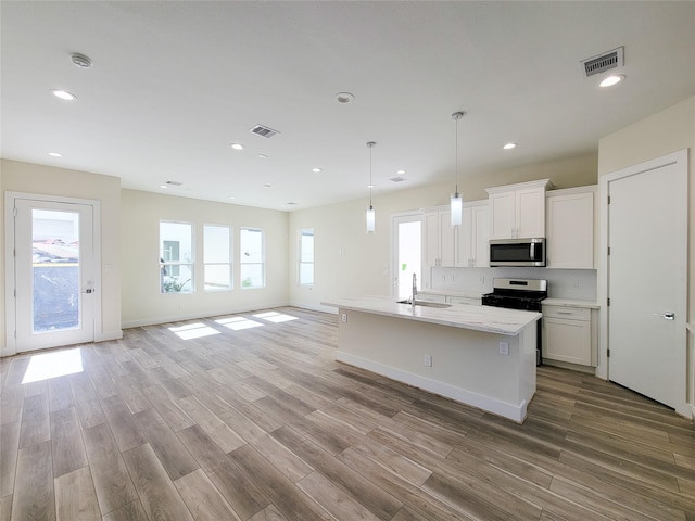 kitchen with stainless steel appliances, sink, decorative light fixtures, white cabinets, and an island with sink