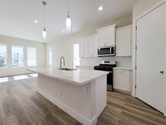 kitchen with appliances with stainless steel finishes, a kitchen island with sink, sink, white cabinetry, and hanging light fixtures