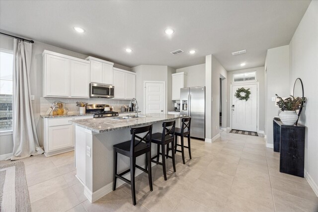 kitchen featuring a kitchen island with sink, sink, appliances with stainless steel finishes, light stone counters, and white cabinetry