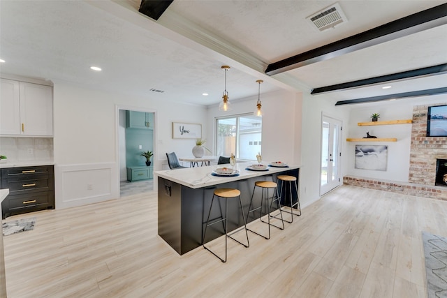 kitchen with white cabinets, light hardwood / wood-style floors, a kitchen bar, and hanging light fixtures