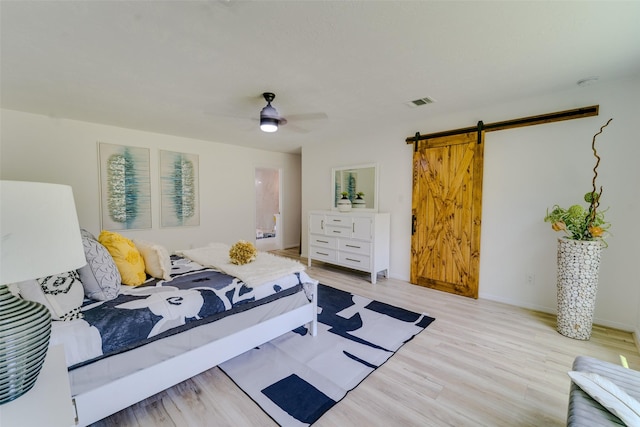 bedroom with ceiling fan, a barn door, and light hardwood / wood-style flooring