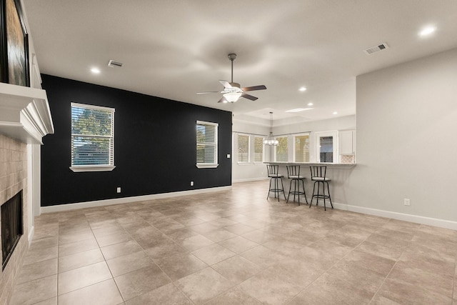 unfurnished living room featuring ceiling fan with notable chandelier and a tiled fireplace