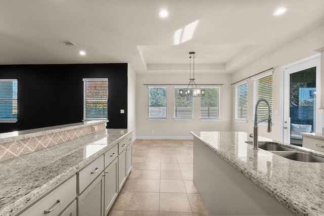 kitchen featuring pendant lighting, an inviting chandelier, sink, a tray ceiling, and light stone counters