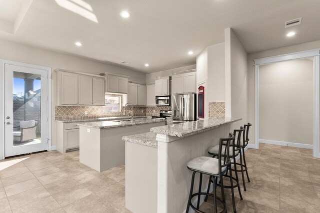 kitchen featuring kitchen peninsula, a kitchen breakfast bar, light stone counters, stainless steel appliances, and a center island with sink