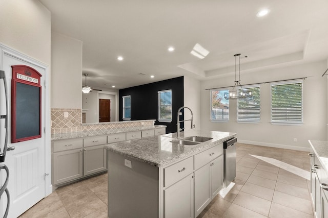 kitchen with decorative backsplash, stainless steel dishwasher, sink, decorative light fixtures, and an island with sink