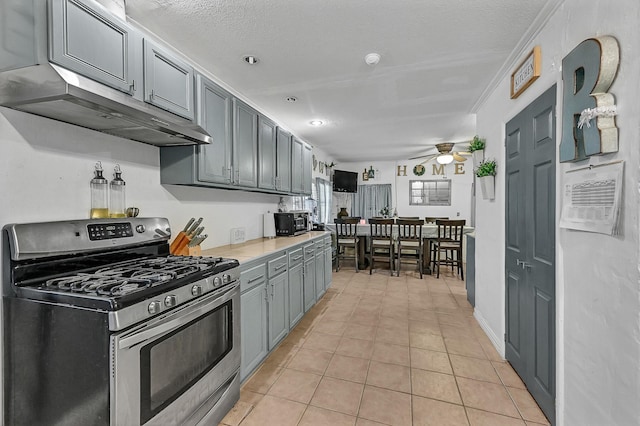 kitchen with ceiling fan, stainless steel gas range, crown molding, a textured ceiling, and light tile patterned flooring