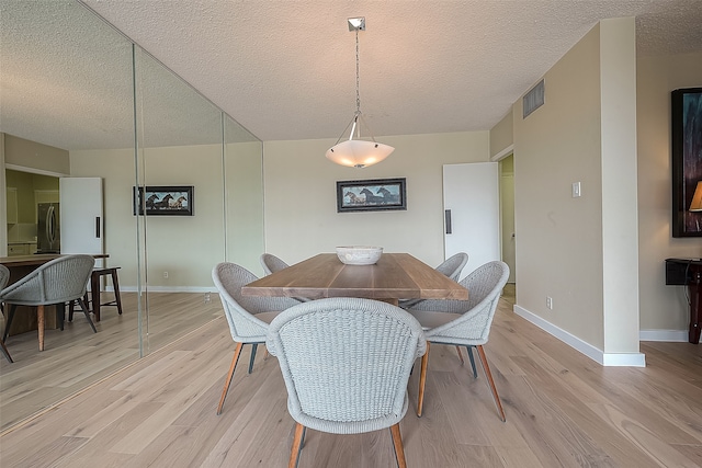 dining space with light wood-type flooring and a textured ceiling