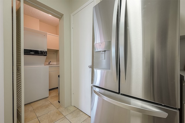 kitchen with white cabinetry, sink, stainless steel fridge with ice dispenser, stacked washer / drying machine, and light tile patterned flooring