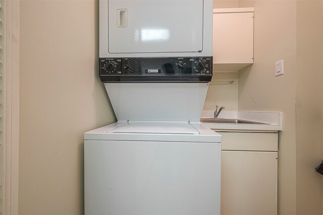 laundry room with cabinets, stacked washing maching and dryer, and sink