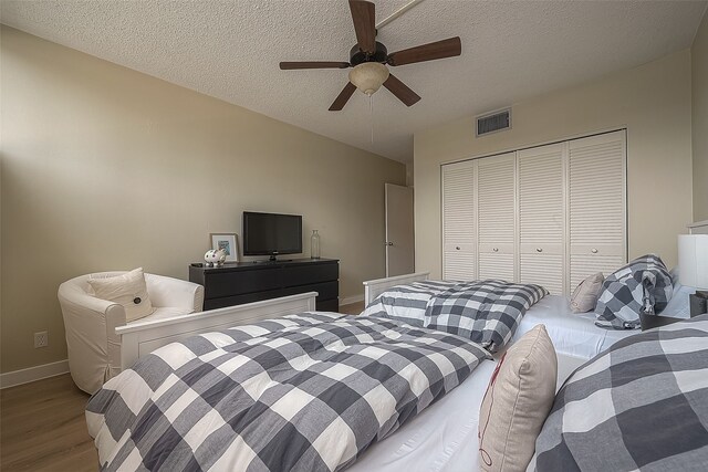 bedroom with a textured ceiling, hardwood / wood-style flooring, a closet, and ceiling fan