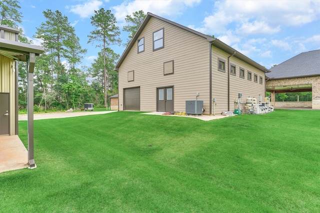 rear view of property featuring a lawn, central AC unit, and a garage