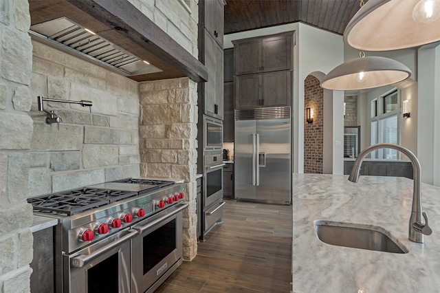 kitchen featuring premium range hood, built in appliances, light stone countertops, and sink