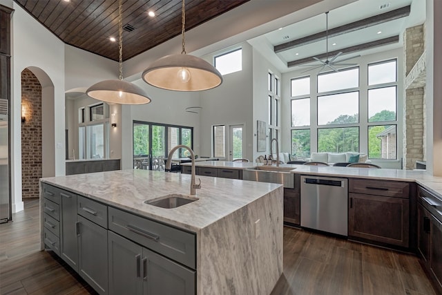 kitchen featuring light stone countertops, sink, decorative light fixtures, a center island with sink, and dishwasher