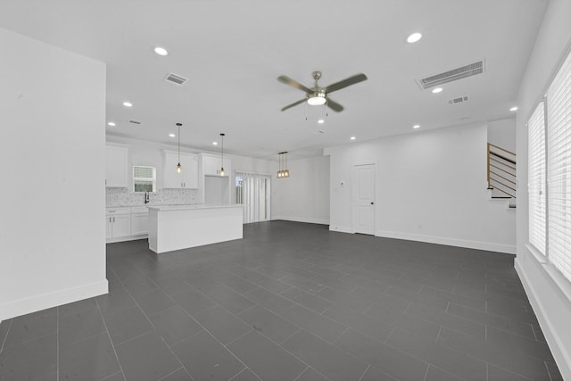 unfurnished living room with dark tile patterned flooring, ceiling fan, and sink