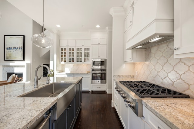 kitchen featuring white cabinetry, stainless steel appliances, light stone counters, decorative light fixtures, and custom range hood