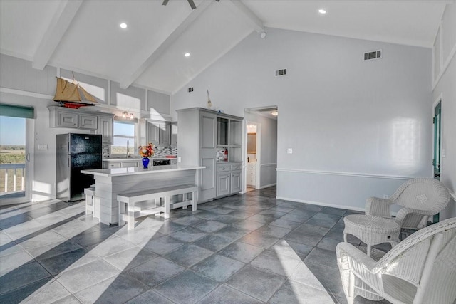 kitchen with gray cabinetry, backsplash, black fridge, sink, and beam ceiling