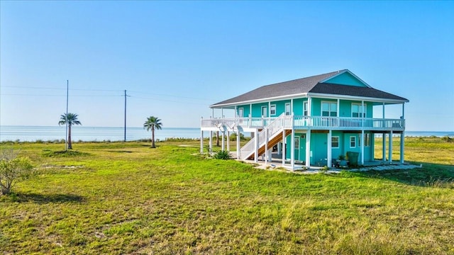 back of property with covered porch, a water view, and a yard