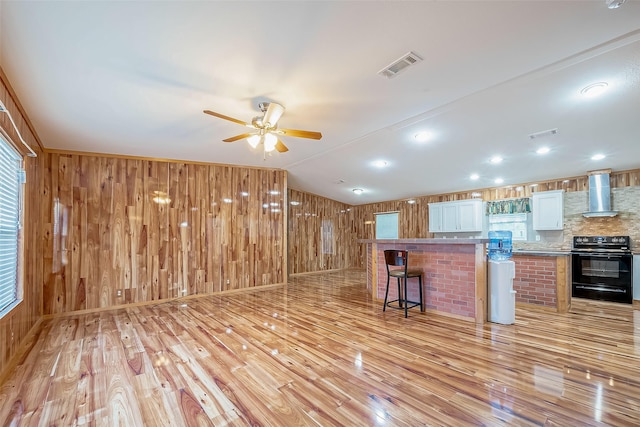 kitchen with wall chimney exhaust hood, a breakfast bar, light hardwood / wood-style flooring, white cabinets, and black electric range oven