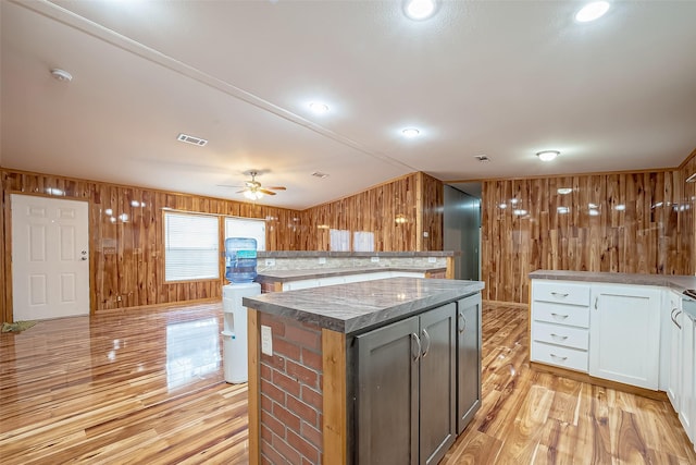 kitchen featuring ceiling fan, a center island, wooden walls, white cabinets, and light wood-type flooring