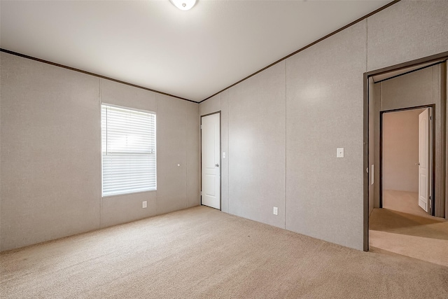 empty room featuring lofted ceiling, light colored carpet, and ornamental molding