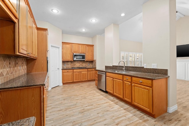 kitchen with backsplash, dark stone countertops, light hardwood / wood-style floors, sink, and stainless steel appliances